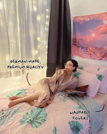 A woman in a pink robe relaxes on a bed featuring a premium German made mattress with washable covers
